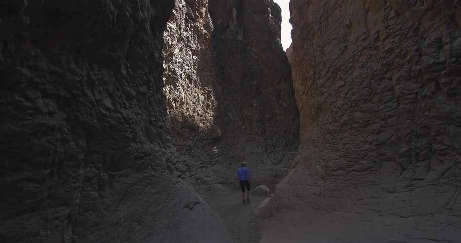 A woman hikes through a barren wash with cliffs rising around her