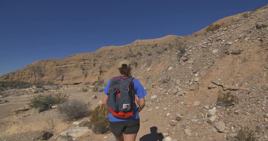 A hiker wearing a backpack is walking through a dirt path with many rocks in a mountain
