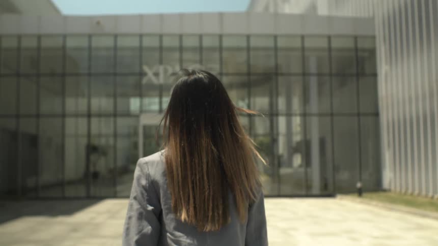 A woman in business attire is approaching the entrance of a large corporate facility during the day