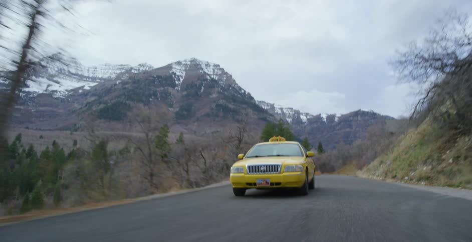 A taxi is traveling on a country road near forest and snowy mountains
