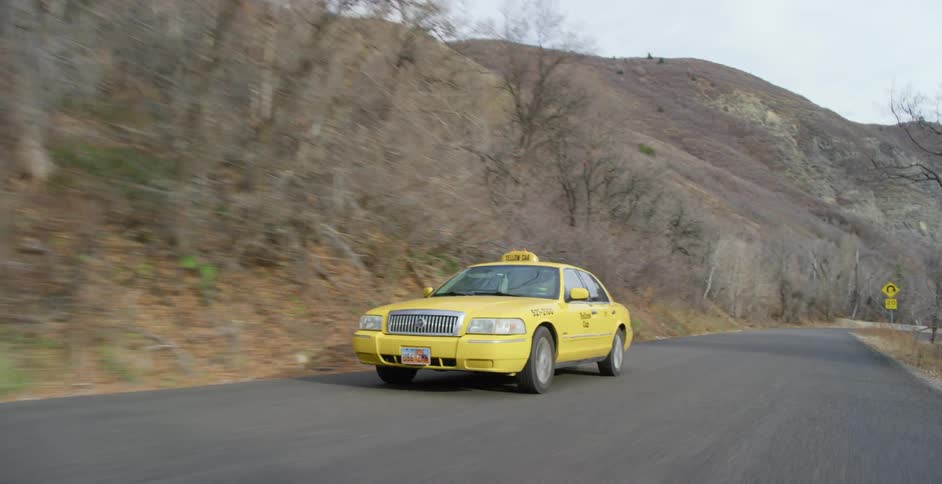 A yellow taxi cab is traveling on a rural road on a sunny day