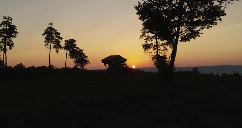Sun sitting on horizon in red sky casts vehicle with portable tent into a silhouette