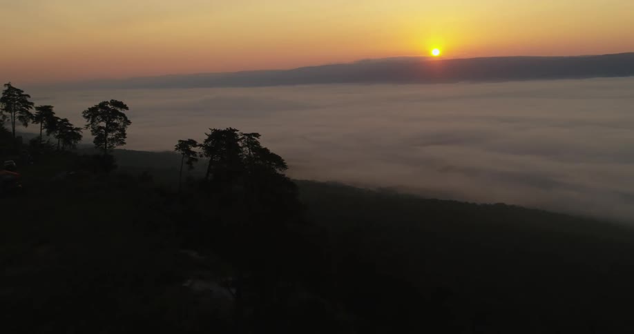 An aerial view of a valley filled with fog at dawn with the sun rising from behind a mountain ridge