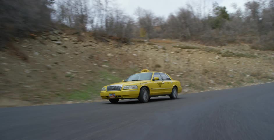 Yellow cab drives along road past forest covered slopes