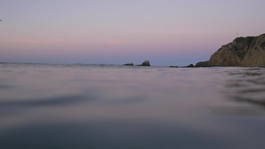 Small sea wave moves across the surface of the sea with cliff and red sky in the background