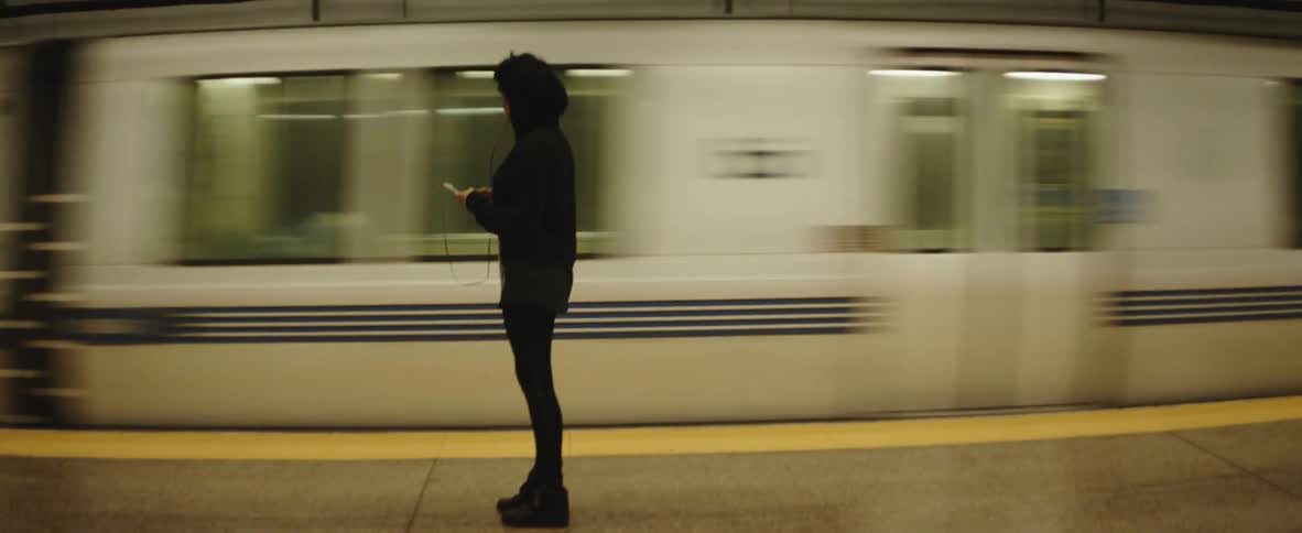 Young woman wearing black clothes watches a subway departs from the station