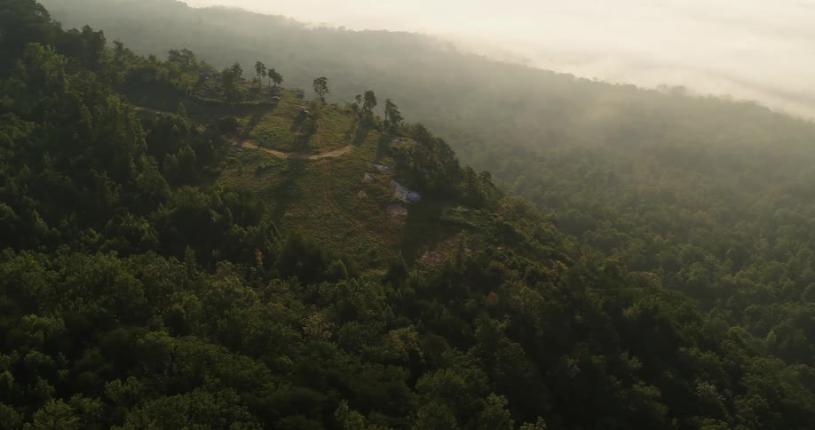 A dirt road ends at a clearing on a mountain ridge with slopes covered in trees