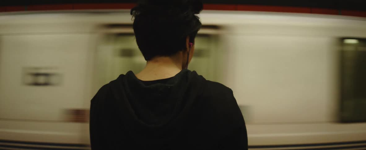 A woman with short dark hair is standing in a subway as a train goes by