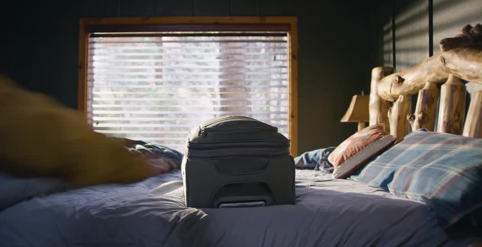 A person grabbing a suitcase off a bed
