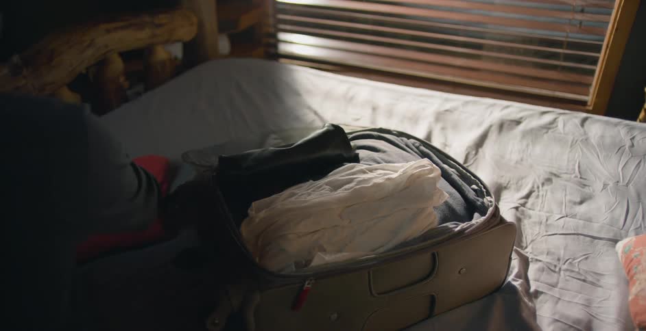 A man packs clothes into his suitcase as it sits on a bed