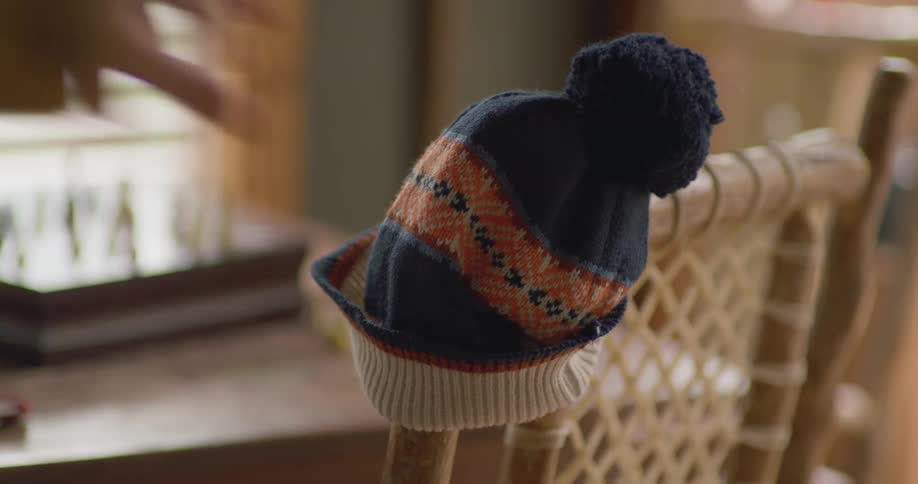 A hat is resting on a chair in a residential room until a hand reaches for and snatches it away