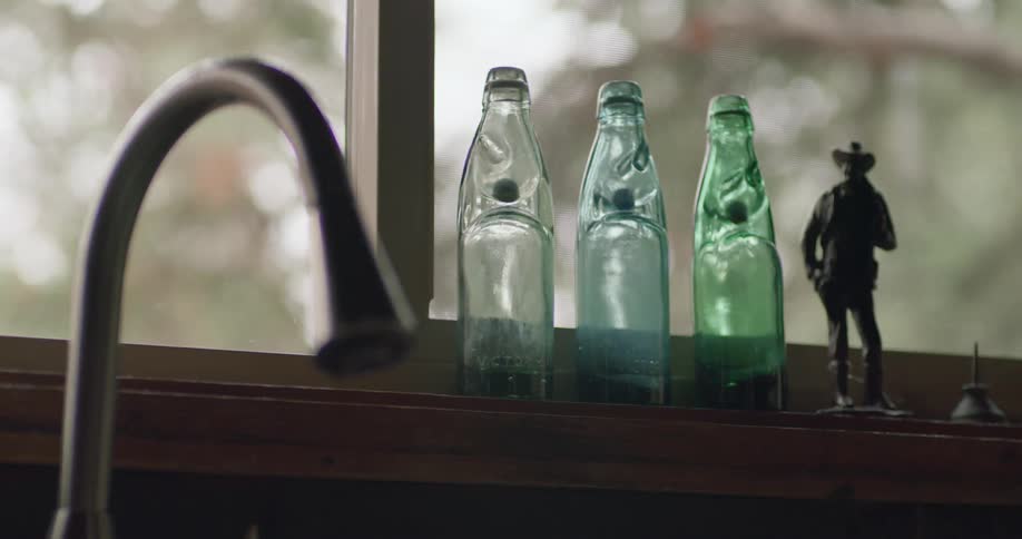 Cowboy figurine and glass bottles sit on windowsill near dripping faucet