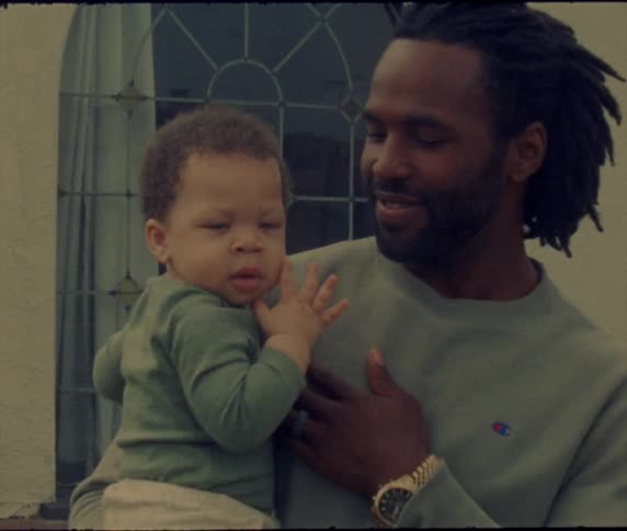 Father lovingly holding his son in his arms in front of a window outdoors caught on vintage film