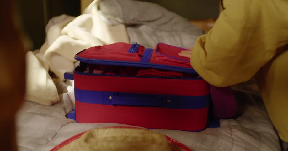 A girl is frantically putting clothes into a suitcase on a bed and then leaves