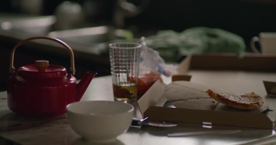 Pizza box and half eaten pizza next to bowl glass and red teapot on table