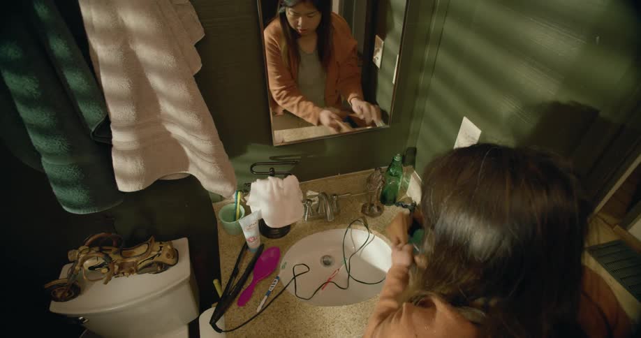 A woman rushes in to a bathroom and quickly packs her toiletries in to a bag