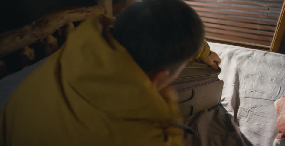 A boy is packing a suitcase that is sitting on a bed and he picks it up and leaves