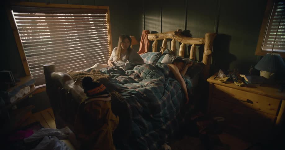 A man and woman sleep in a bed when suddenly the woman sits up looks around and wakes her husband and they both quickly jump out of bed and put clothes on