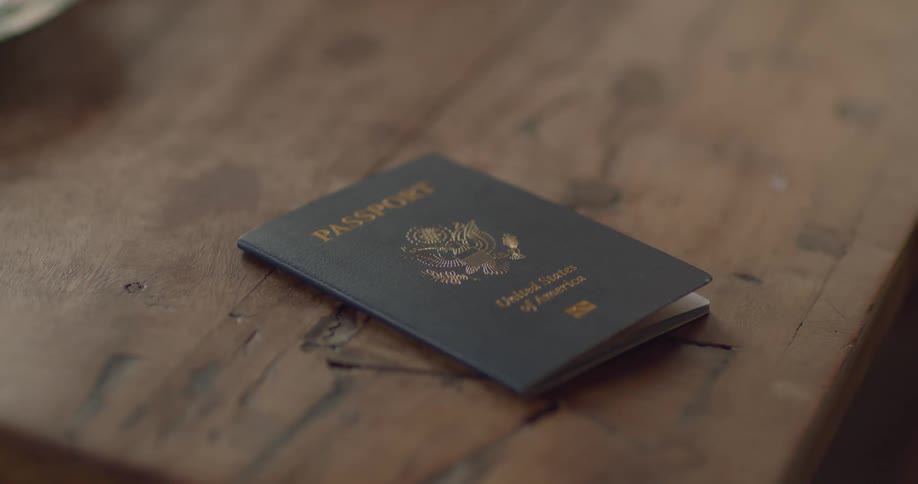 A man reaches for and slides a passport off an indoor wooden table in the daytime