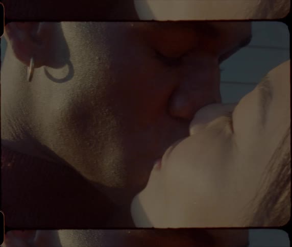 A woman reaches up and kisses a man outside as he gazes at her with love