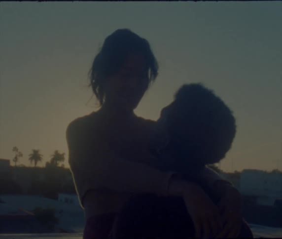 A woman stands over her boyfriend as they hug on the beach