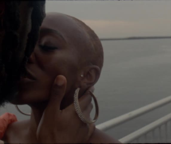 A man and woman are standing at a lookout point by a lake while kissing and looking into each others eyes in the evening