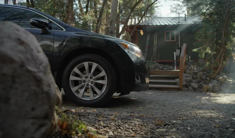 A black car stops in front of a little house in the woods