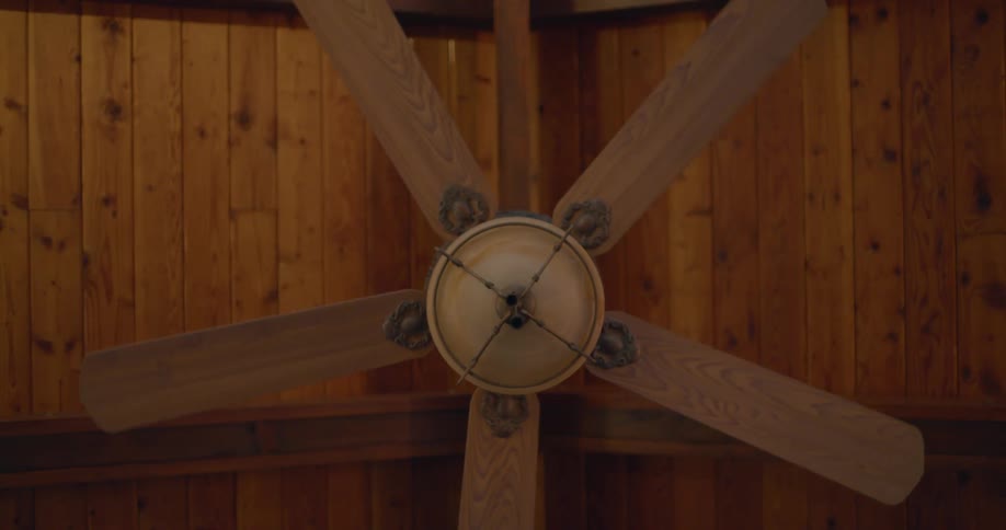 A ceiling fan hanging from a hardwood paneled ceiling turns slowly