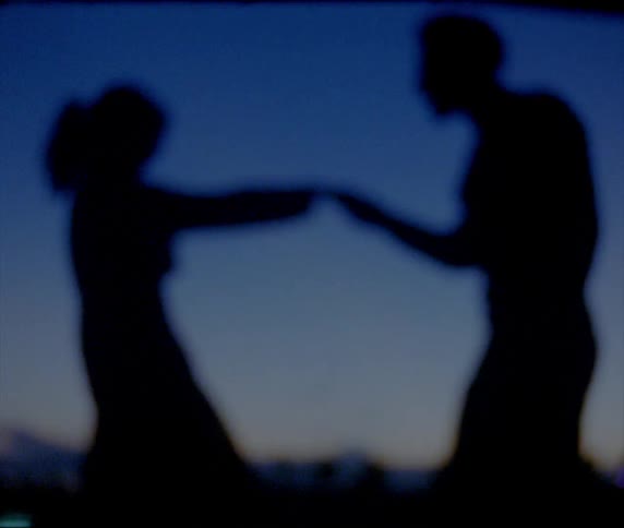 A man twirls his girlfriend around and pulls her in for a hug and kiss as they stand outside