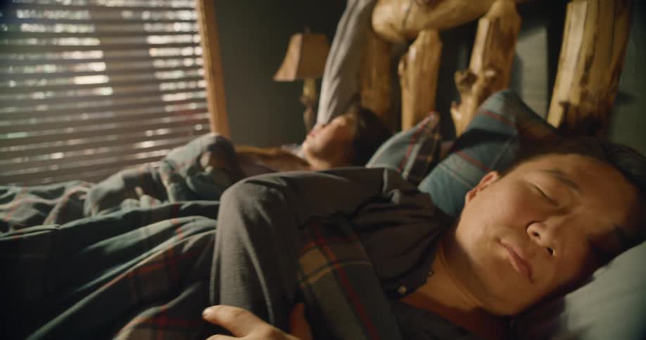 A man and woman asleep in a bed with a wooden post headboard
