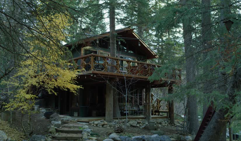 A two story cabin with large balconies sits isolated in the woods