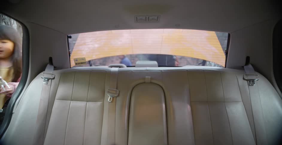 View from the back seat of a car as a man opens the trunk and puts something inside and kids get in the car