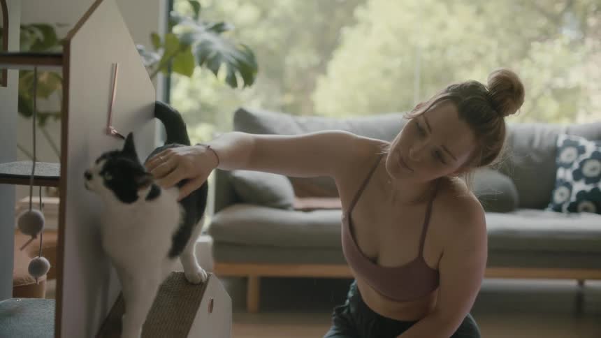 A woman pets her cat as it sits on a scratcher