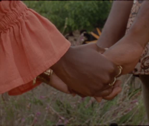 Two women with dress and orange blouse hold hands with rings in the garden