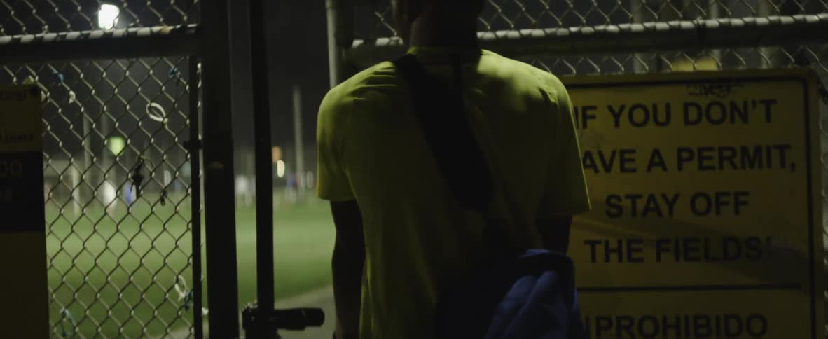 A man carries a duffle bag as he walks through a chain gate to a soccer stadium