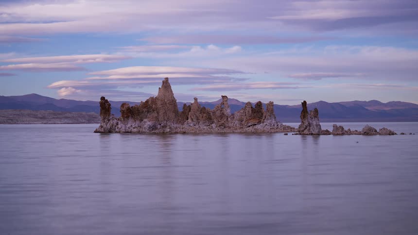 Time lapse of clouds passing over distant mountains and rocks in lake
