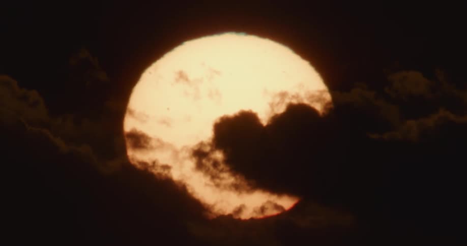 A zoomed in view of the sun rising behind the clouds at dawn