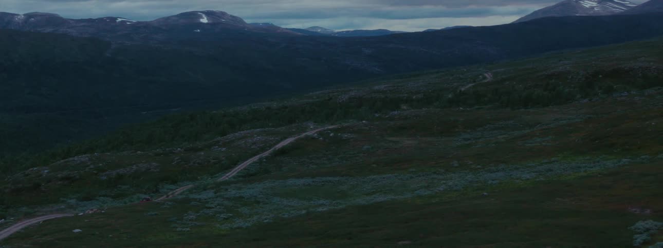 An aerial view following a pickup truck traveling on a dirt road on a forested mountain at dusk evening