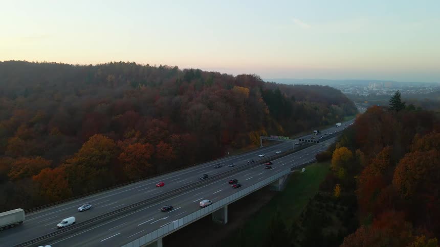 Heavy traffic passes down a freeway surrounded by forest and leading in and out of downtown