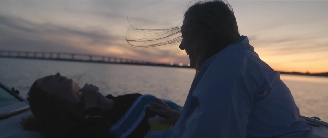 Happy friends resting on a boat laugh while sailing on a lake at sunset