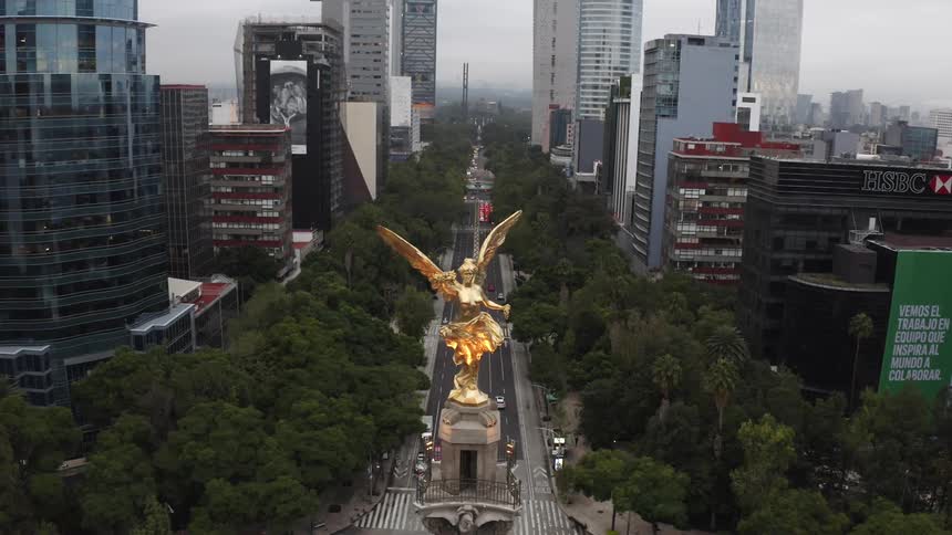 An aerial view of Angel of Independence in front of high rise office buildings with cars driving on streets and pedestrians walking
