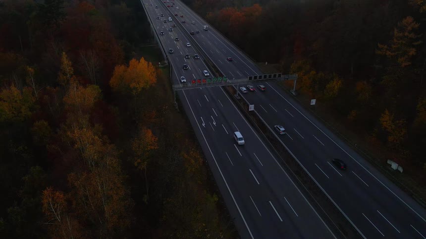 Vehicles speed along a busy highway that runs past a forest