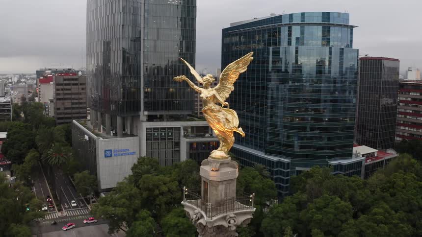 Gold statue of angel tops tower with fenced viewing platform in downtown near busy intersection