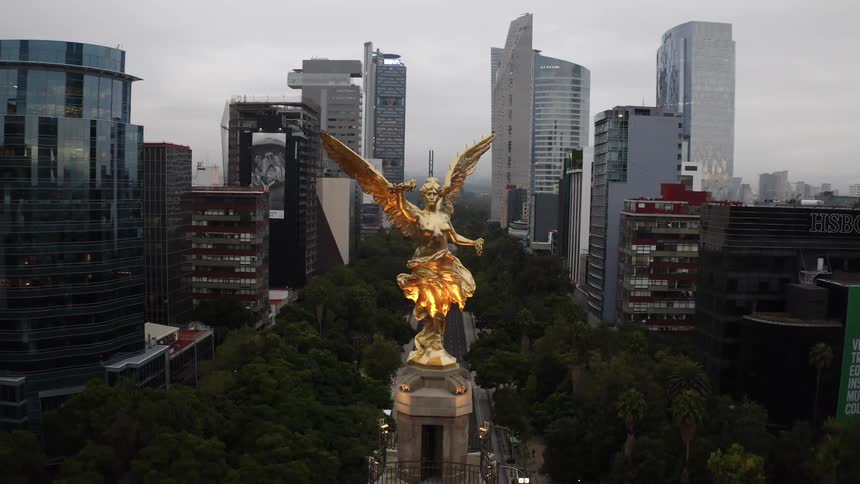 An aerial view of a statue in a downtown area with office buildings and cars driving and pedestrians walking