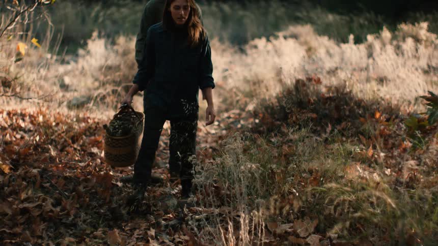 A woman carries a tote filled with weeds and flowers as she and her partner walk through a field