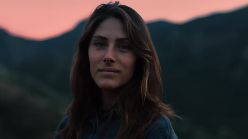 Woman smiles slightly as she poses outdoors under red sky with mountain in background