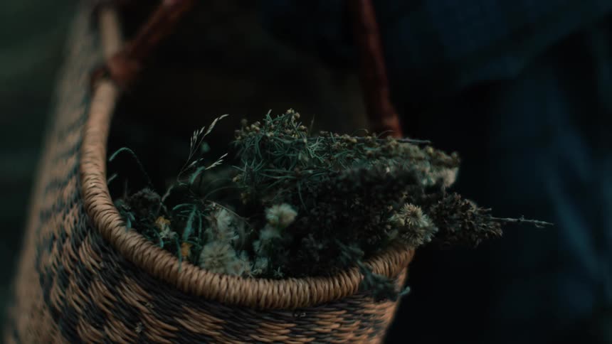 A woman places fresh picked flowers into a woven tote