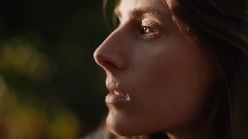 Woman slowly opens her eyes to stare as sun casts part of her profile in shadow