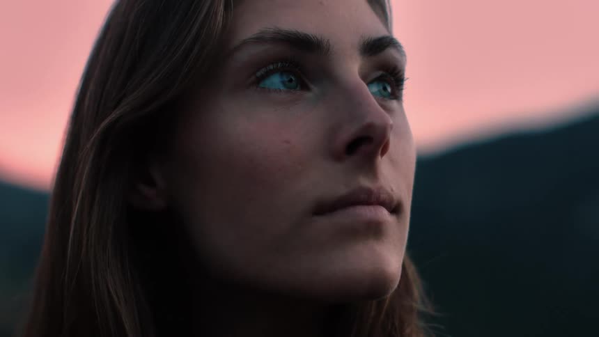 A woman is standing outside looking around under a pink sky