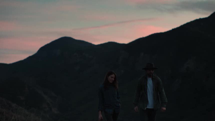 A man and woman look into each others eyes before walking away as they hike near mountains